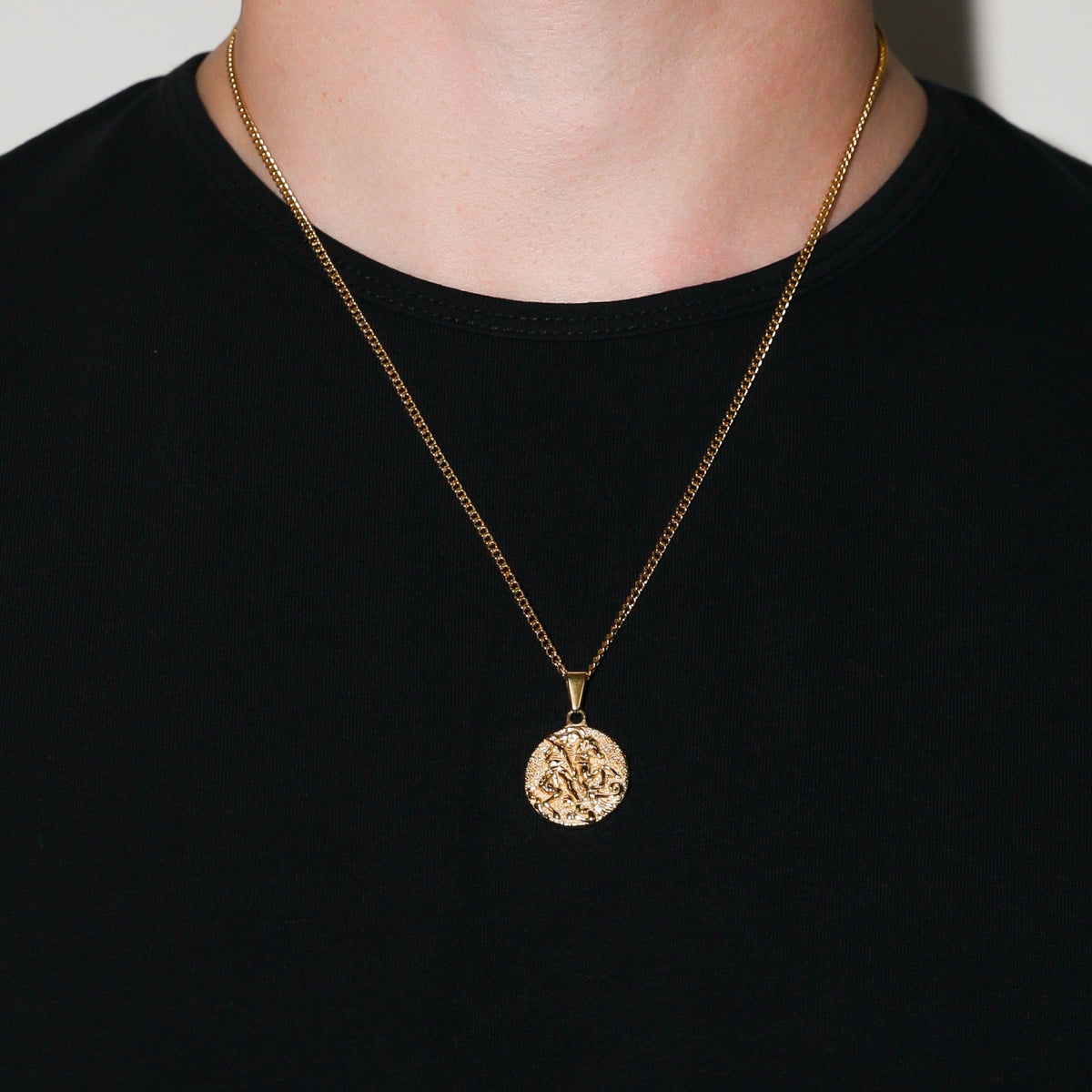 Gold coin pendant necklace worn on chest over black crewneck shirt