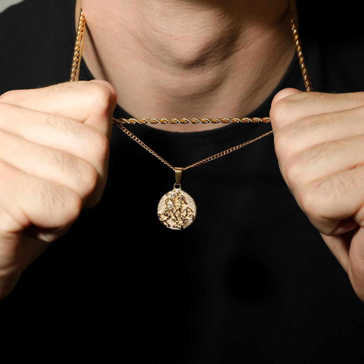 Gold coin pendant necklace with hands holding chain, round St. George medal visible