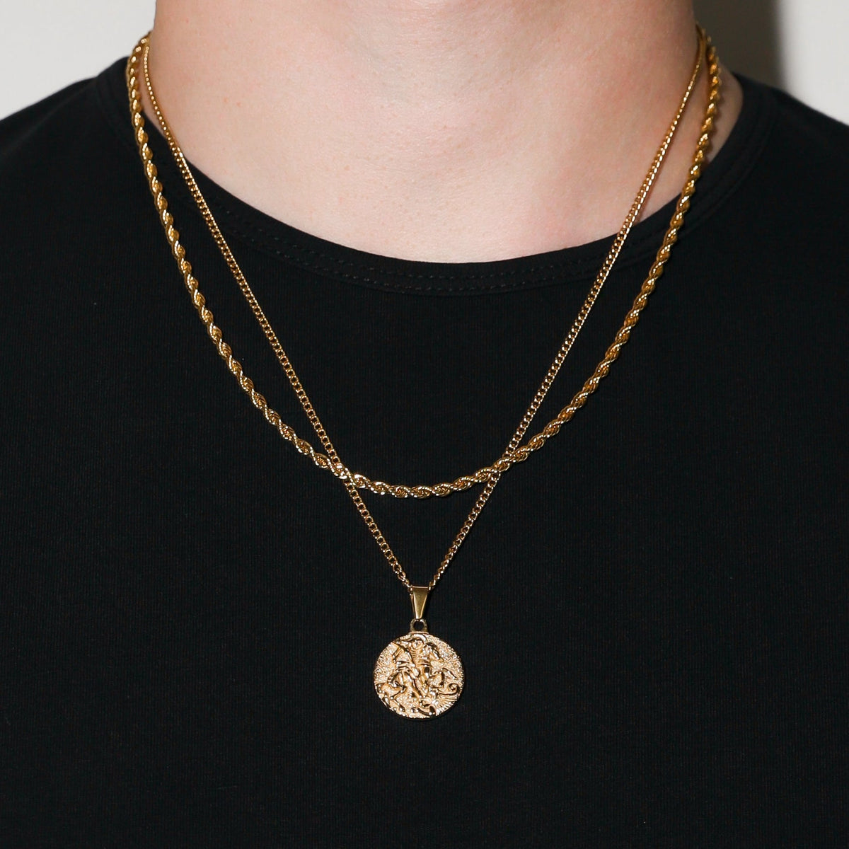 Gold coin pendant necklace hanging at center chest with round St. George medal