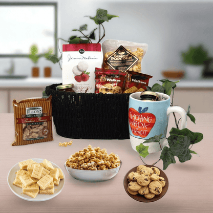 Gift basket with black woven basket, mug, and assorted snack packages and cookies.
