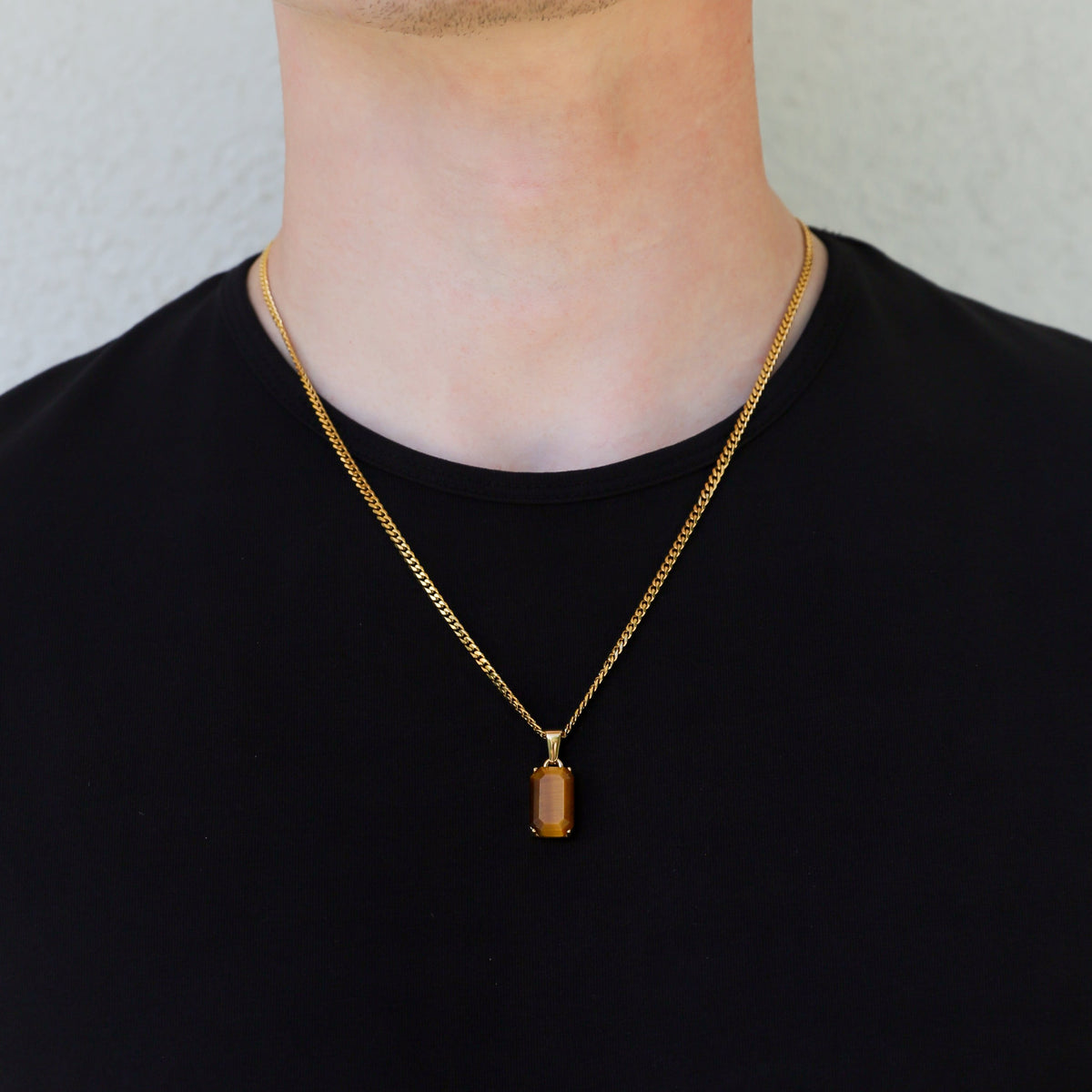 Gold tiger eye stone pendant necklace on a linked chain, worn on a man in black