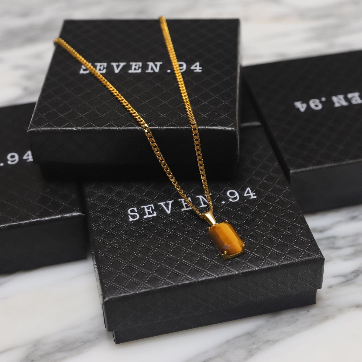Gold tiger eye stone pendant on chain with black gift boxes in view
