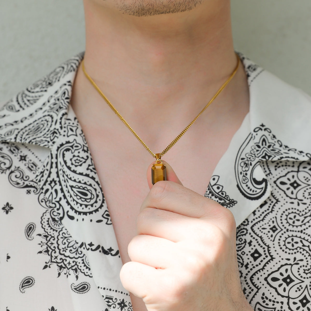Gold tiger eye pendant on linked chain, hand holding the clasp near the neck