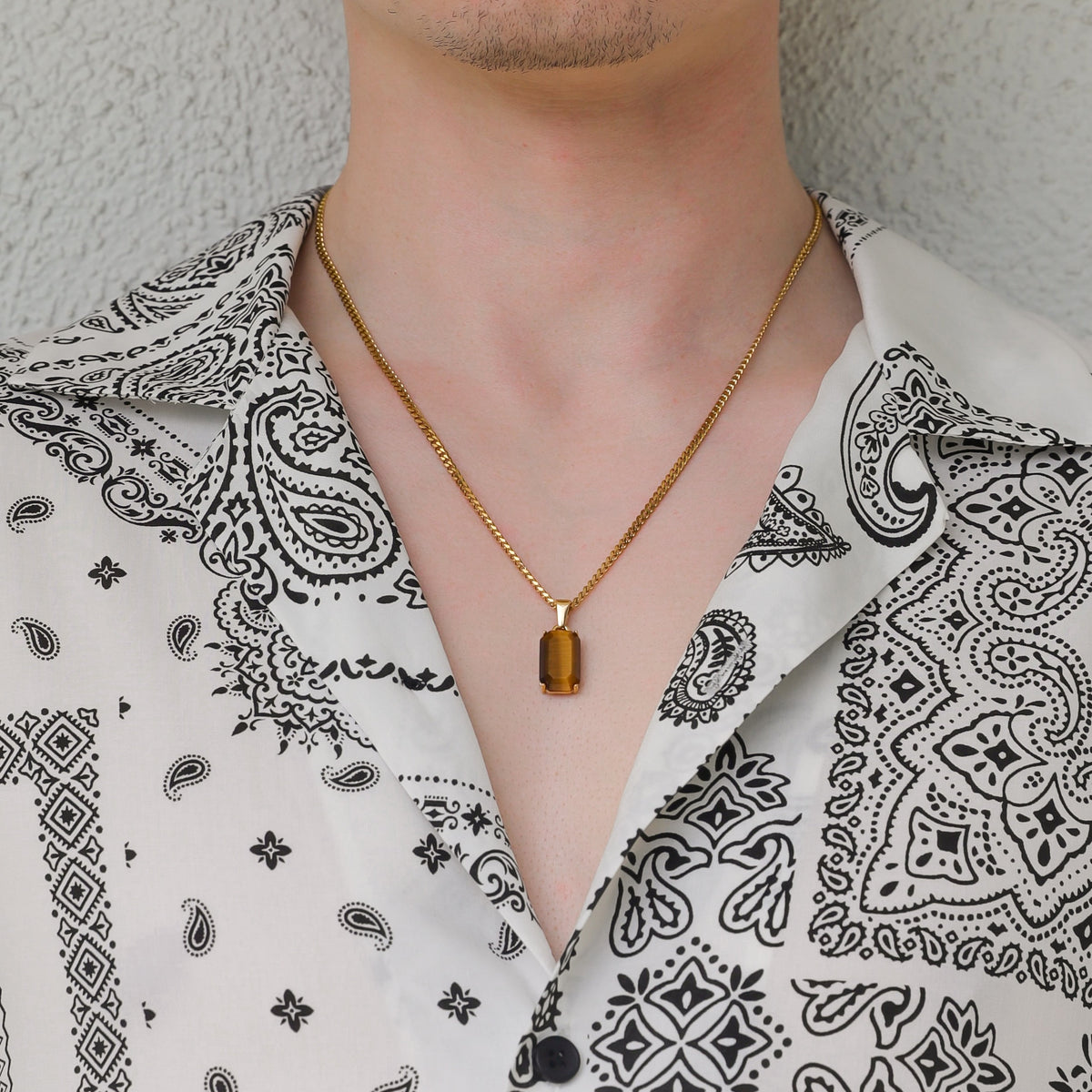 Gold tiger eye stone pendant necklace on linked chain worn over a paisley shirt