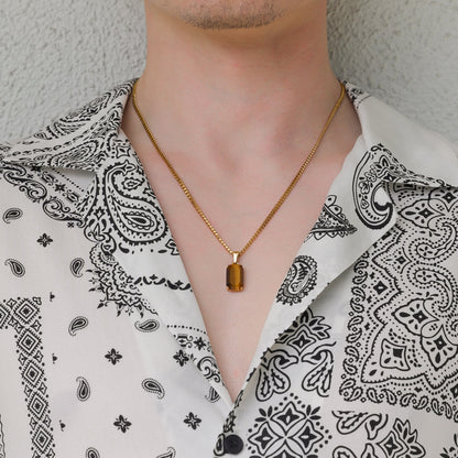Gold tiger eye stone pendant necklace on linked chain worn over a paisley shirt