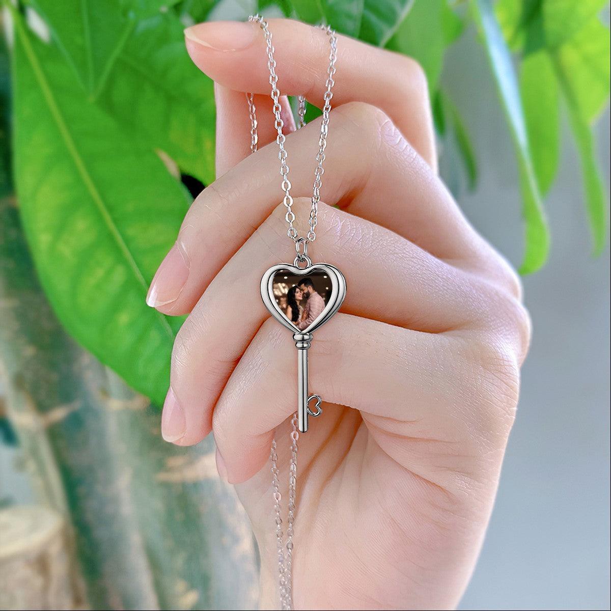 Silver-tone heart locket and key pendant photo necklace on a chain, held in hand