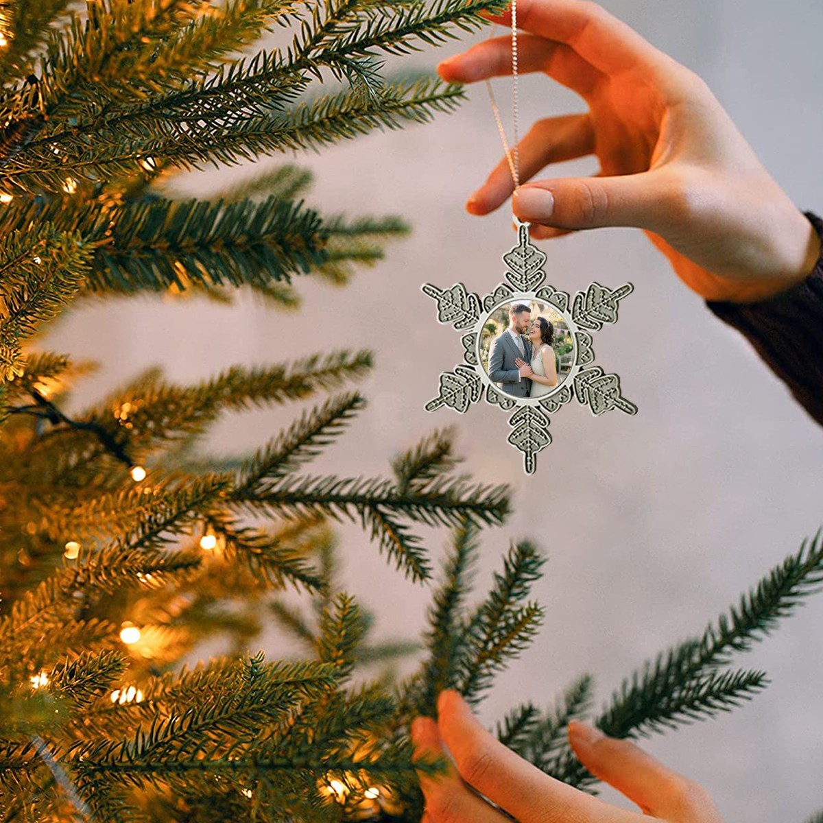 Silver snowflake-style photo ornament on a tree branch, held by a hand.