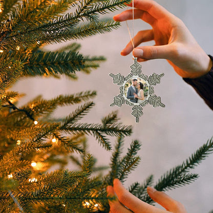 Silver snowflake-style photo ornament on a tree branch, held by a hand.