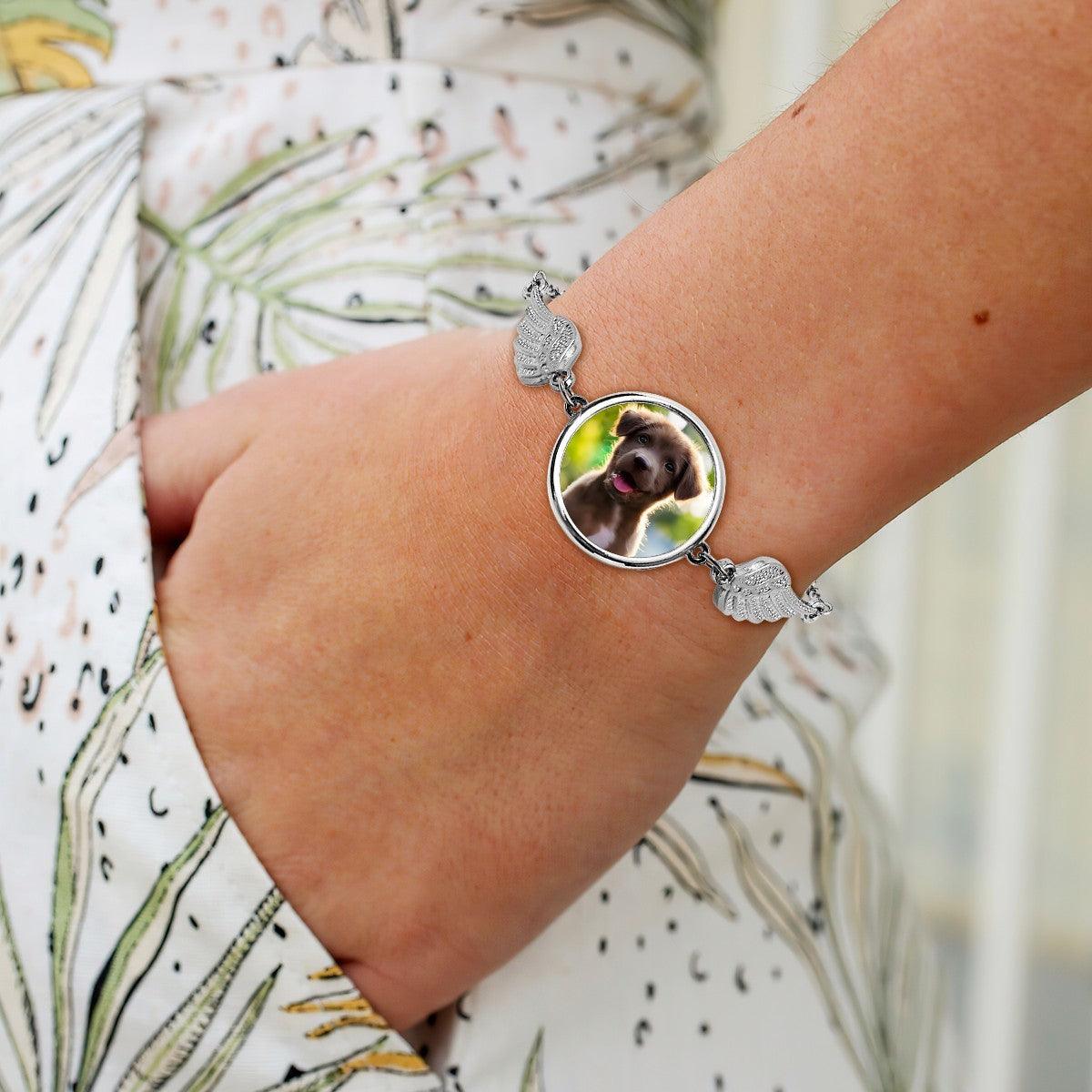 Silver pet memorial photo bracelet with round dog locket and angel wing charms on wrist