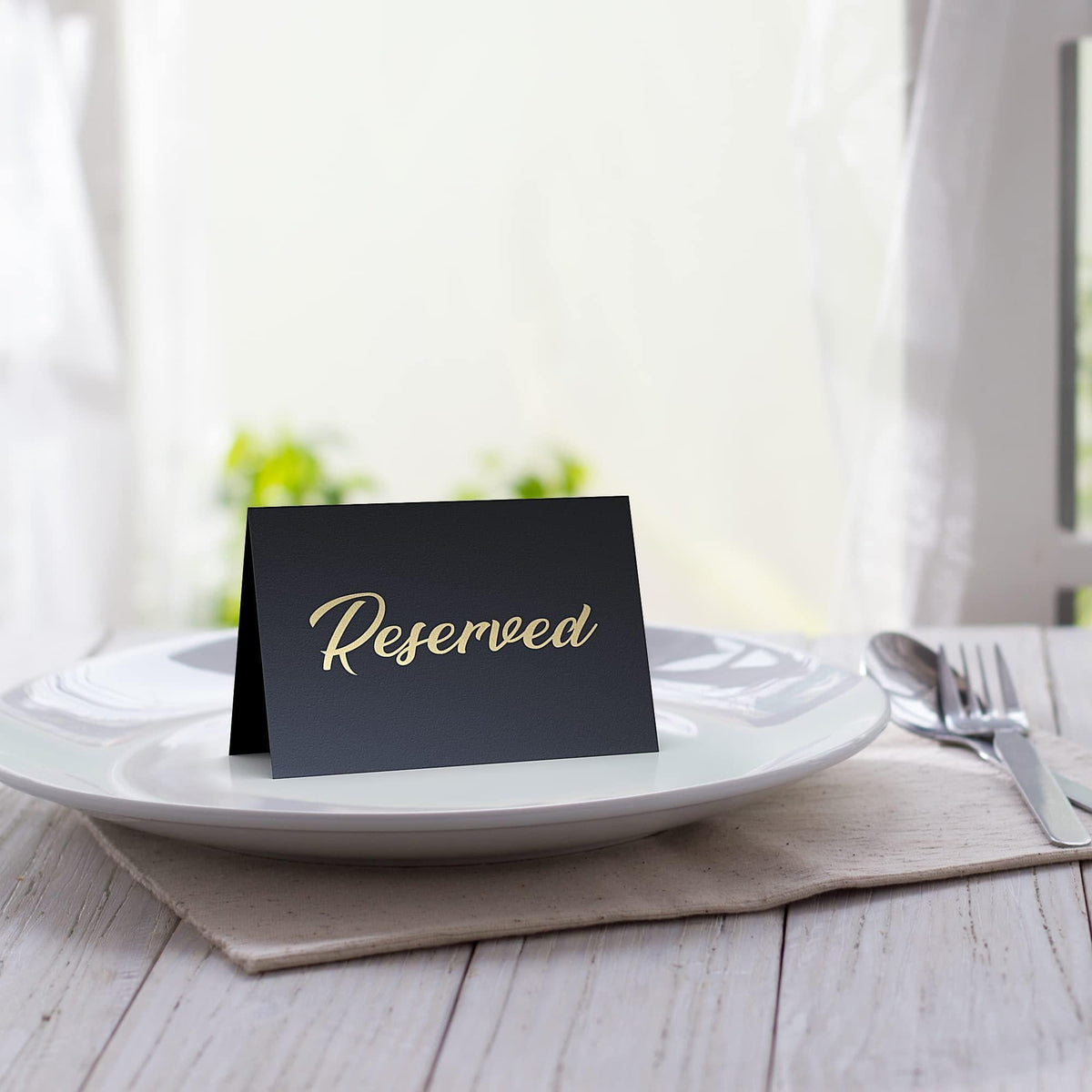 Black tent sign on a plate with gold-foil “Reserved” lettering