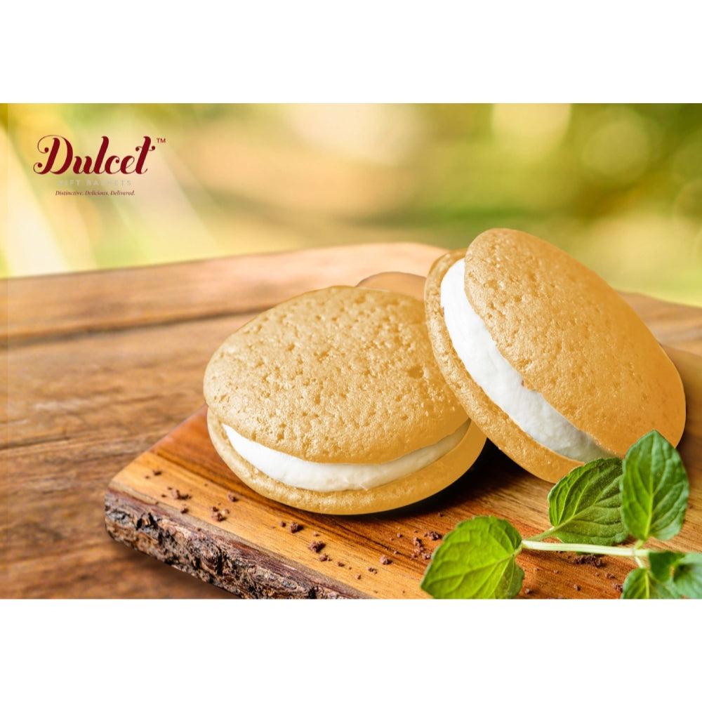 Two round cookies with white filling on a wooden board, with green mint leaves