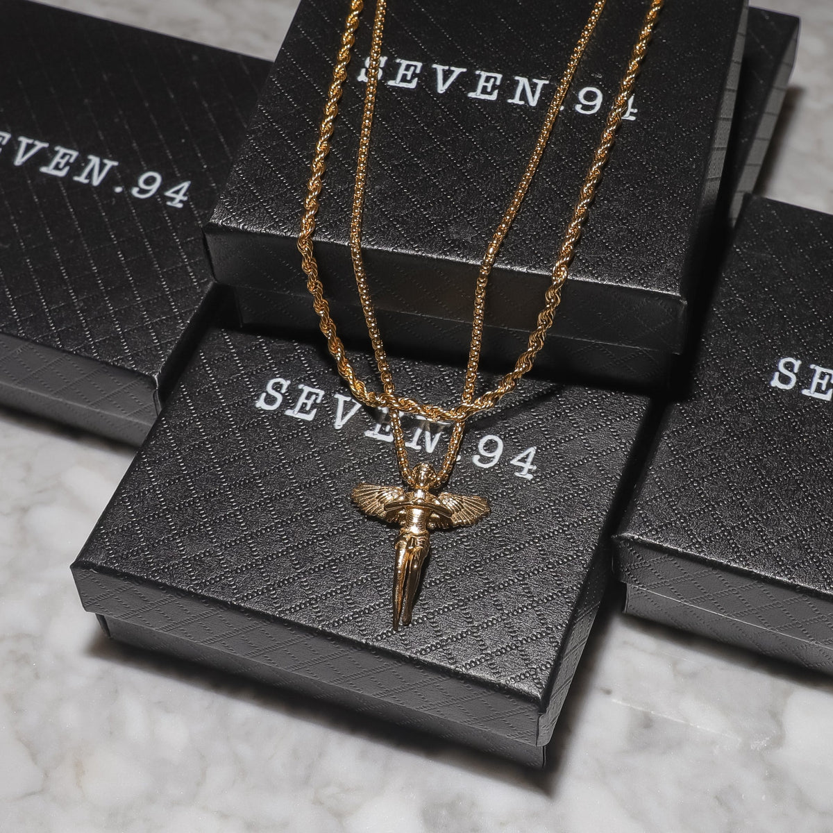 Gold guardian angel rope chain pendant displayed on jewelry boxes