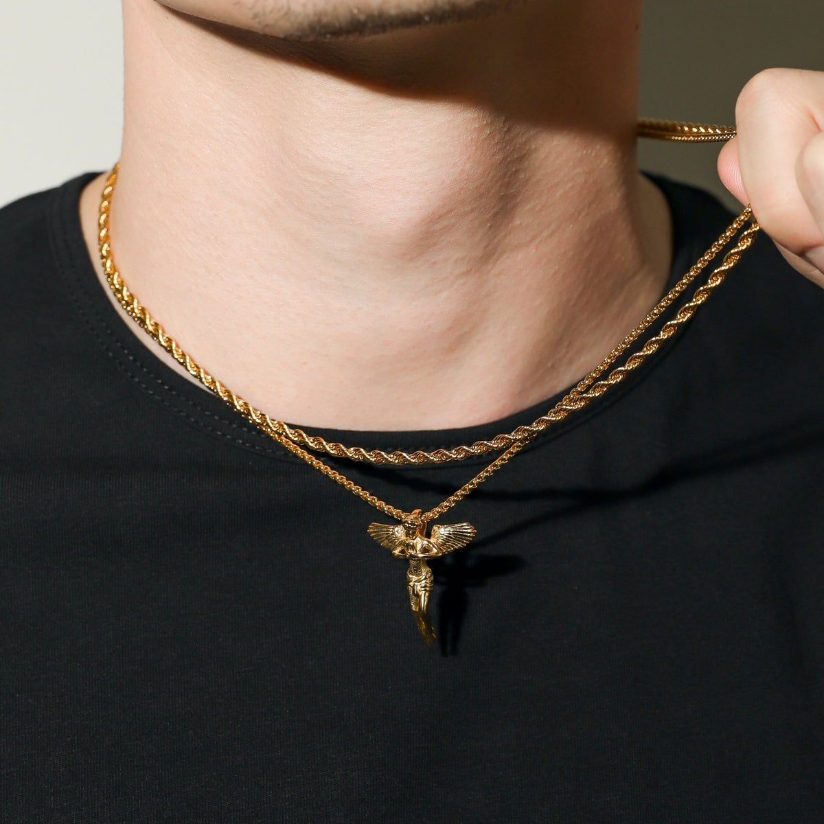 Gold rope chain necklace with guardian angel pendant, close-up at the collar