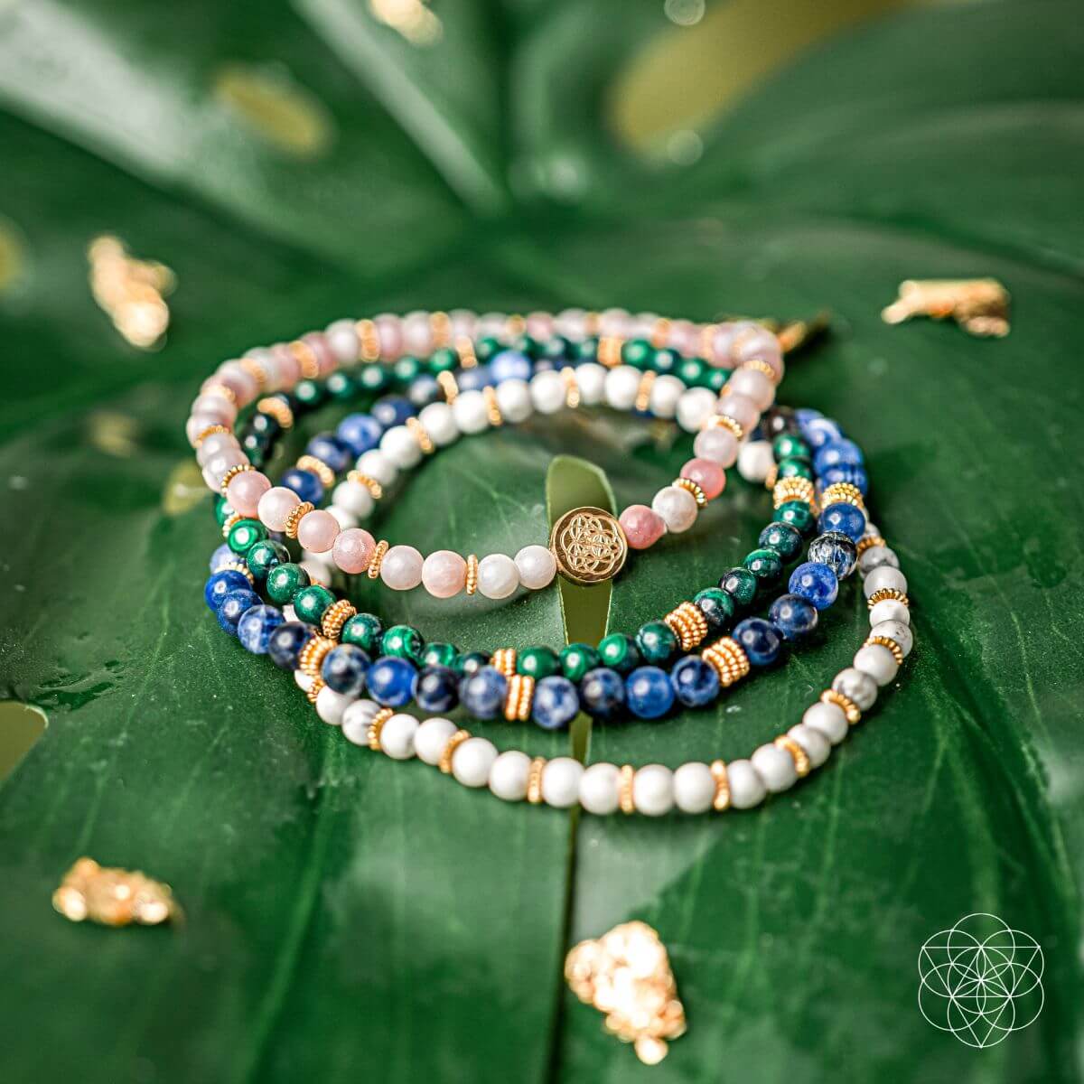 Stack of beaded bracelets with blue, green, white, and pink beads and gold charm