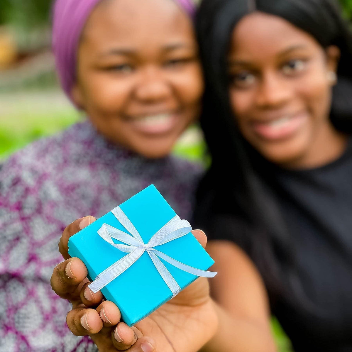 Small turquoise gift box with white ribbon bow held in hands