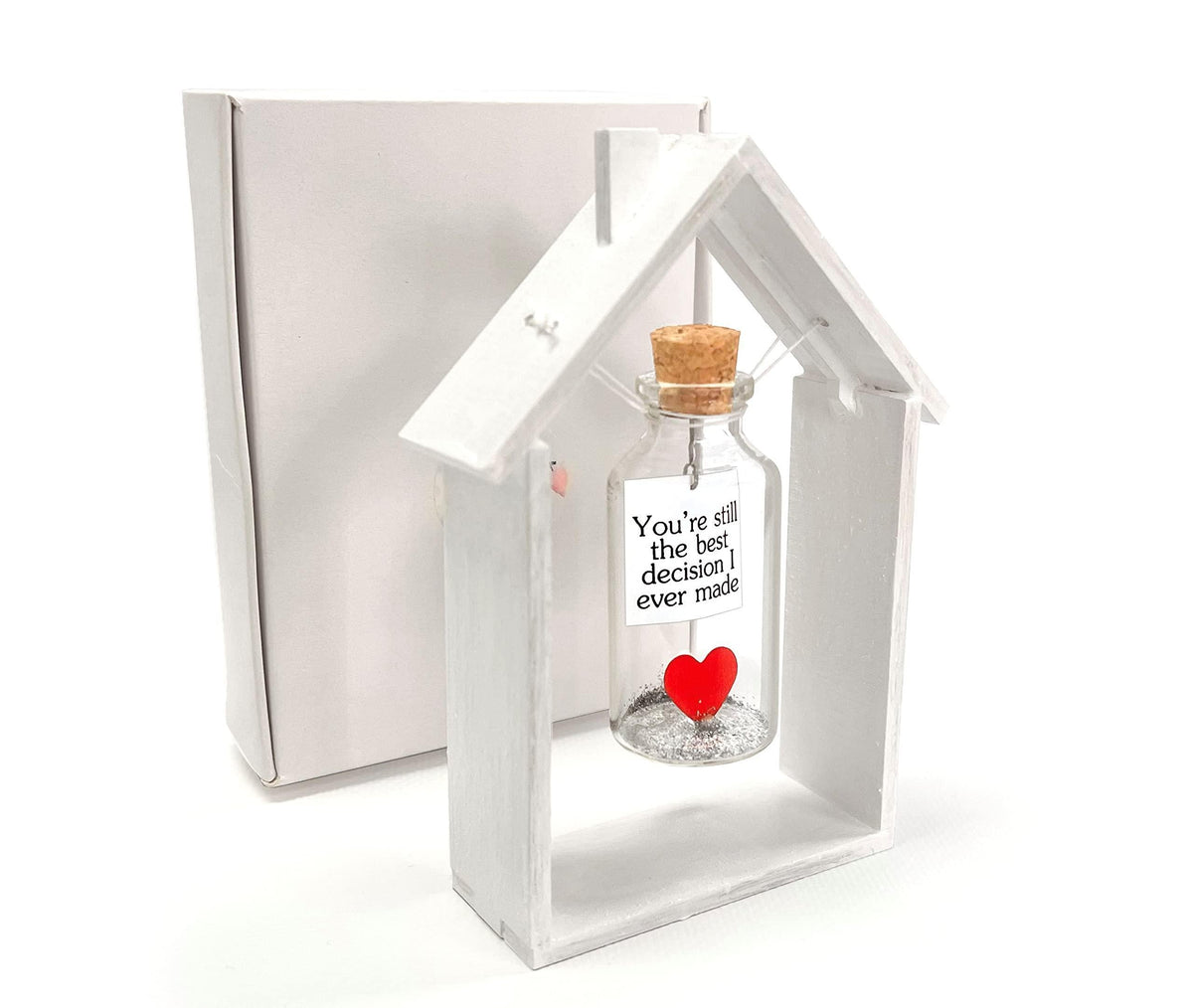Heart message bottle in white wooden house frame beside gift box, red heart on bottle