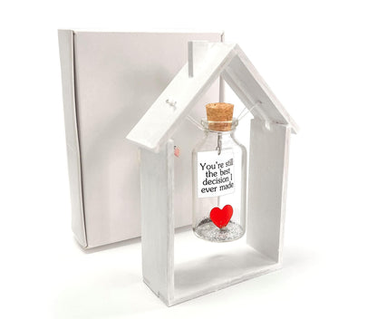 Heart message bottle in white wooden house frame beside gift box, red heart on bottle