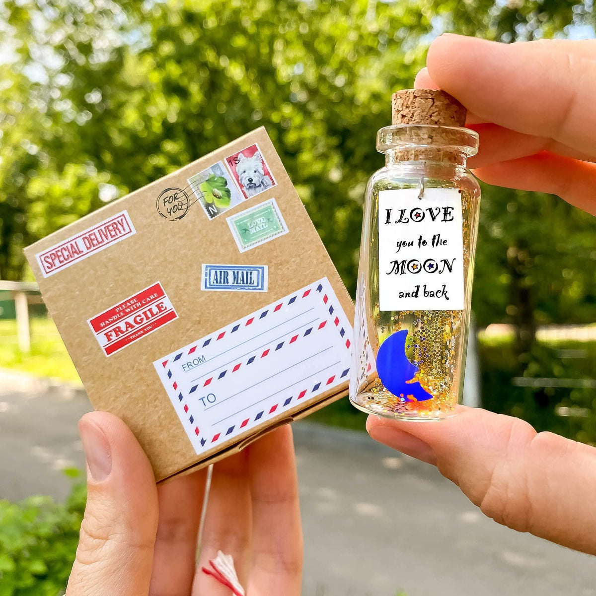 Mini corked keepsake bottle with moon label held near craft gift box outdoors