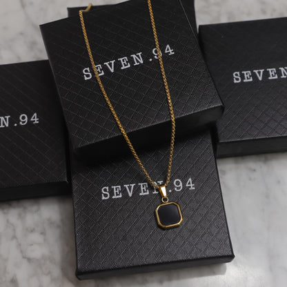 Gold-tone black octagon onyx pendant on a layered chain, displayed on boxes