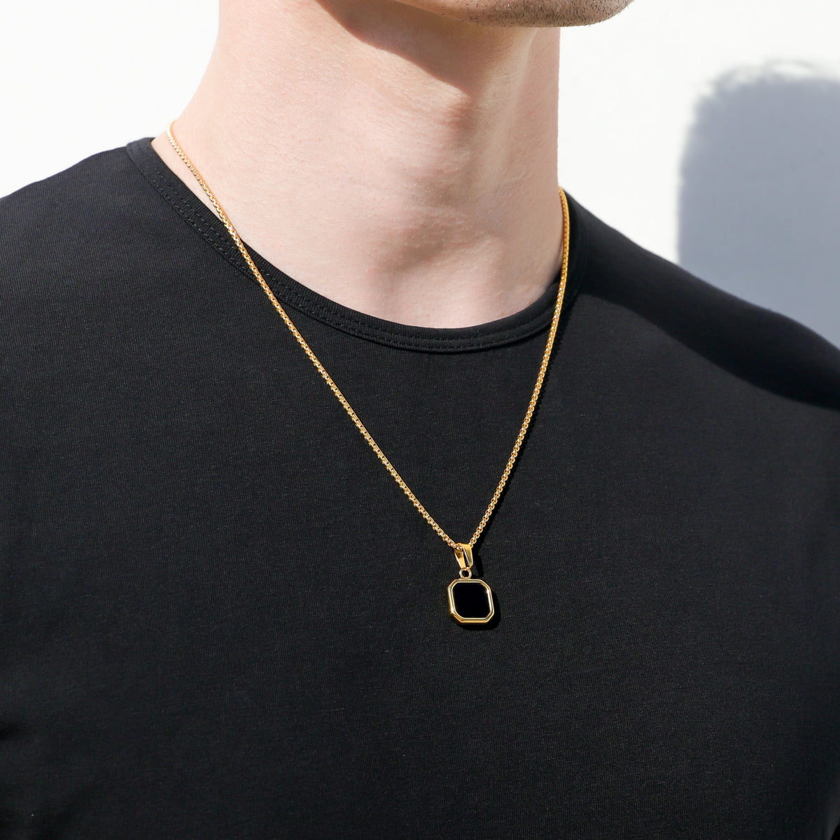 Gold-tone chain necklace with black octagon pendant hanging from the collar