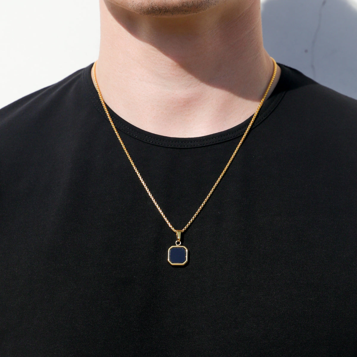 Gold-tone chain necklace with black octagon pendant centered on the chest
