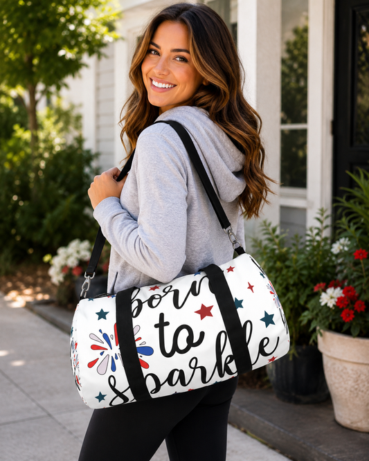 White duffel bag with black straps and “born to sparkle” text, stars and firework prints