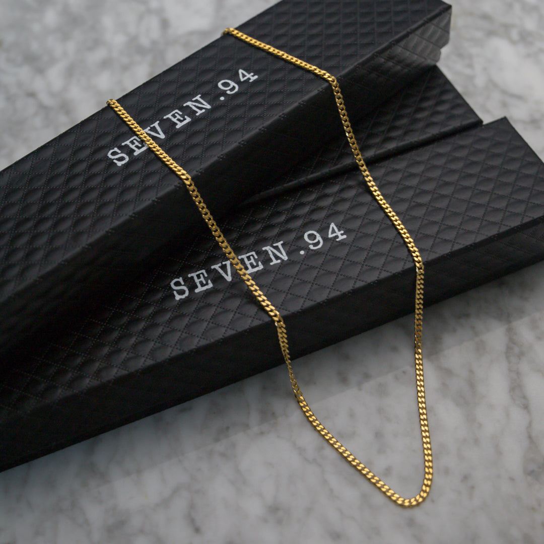 Gold Cuban link chain necklace draped over black jewelry box packaging.
