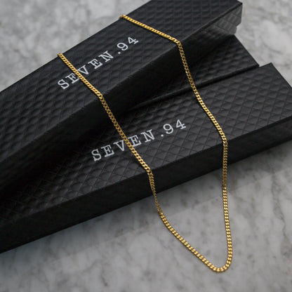 Gold Cuban link chain necklace draped over black jewelry box packaging.