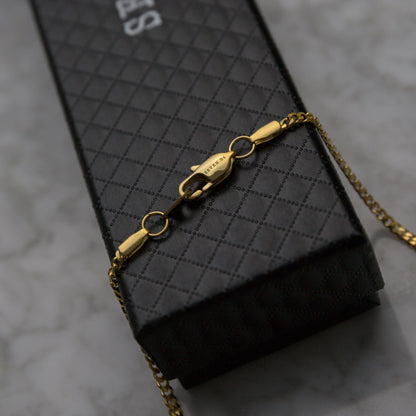 Gold Cuban link chain necklace with clasp, shown resting on packaging.