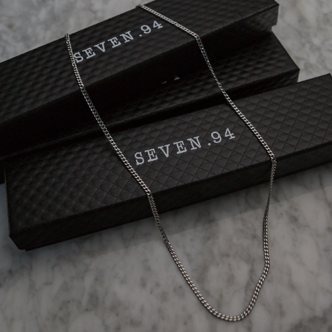 Silver-tone Miami Cuban link chain necklace laid over black jewelry boxes