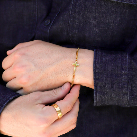 Gold cross charm bracelet worn on wrist over dark blue shirt sleeve