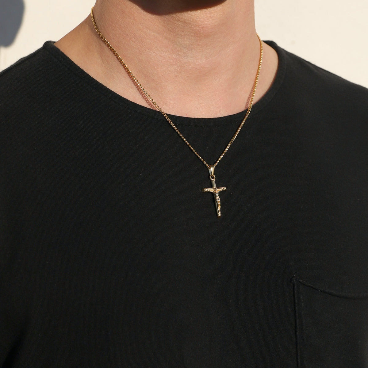 Gold crucifix pendant on curb chain, centered on chest, worn with black crewneck