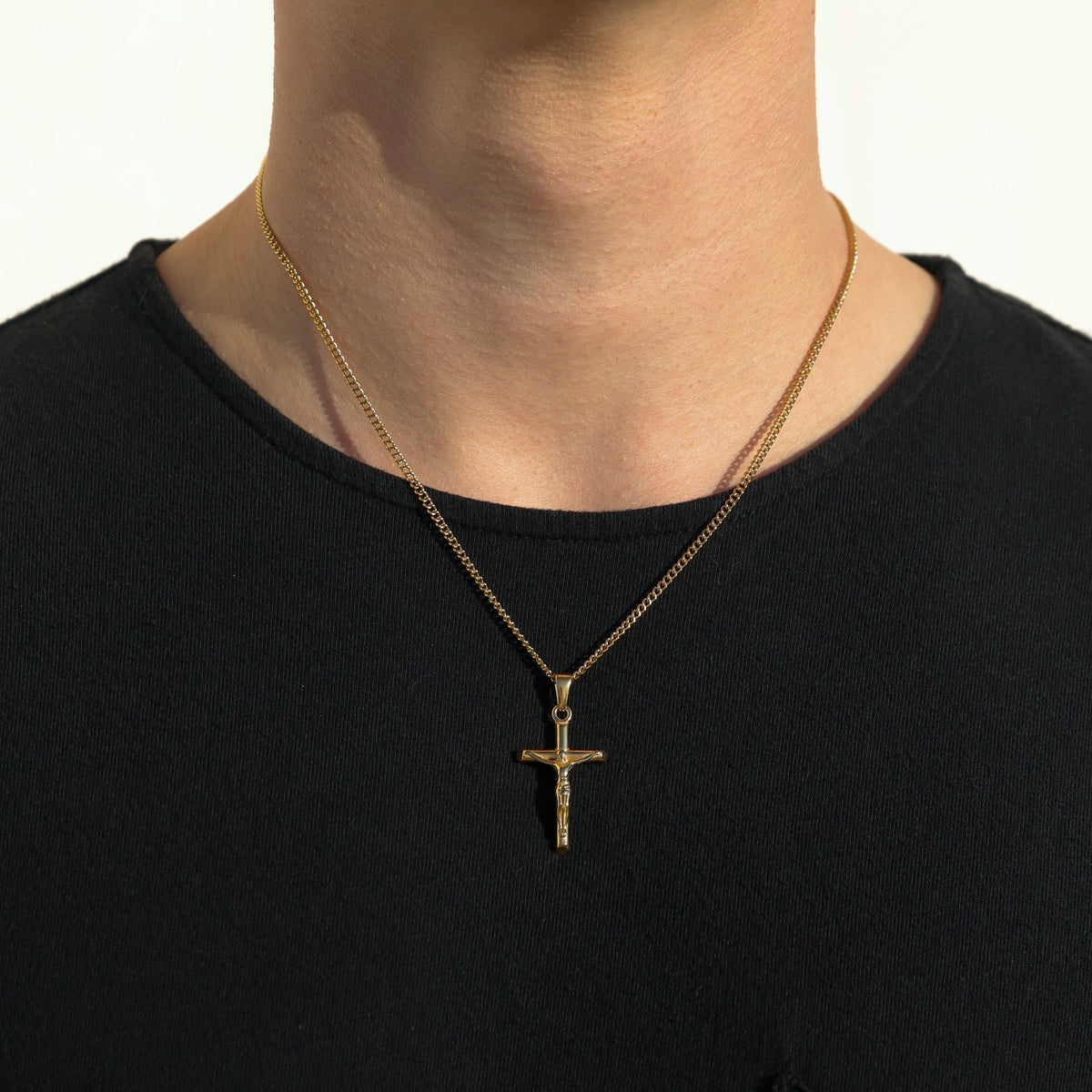 Gold crucifix pendant necklace on curb chain worn on chest over black shirt