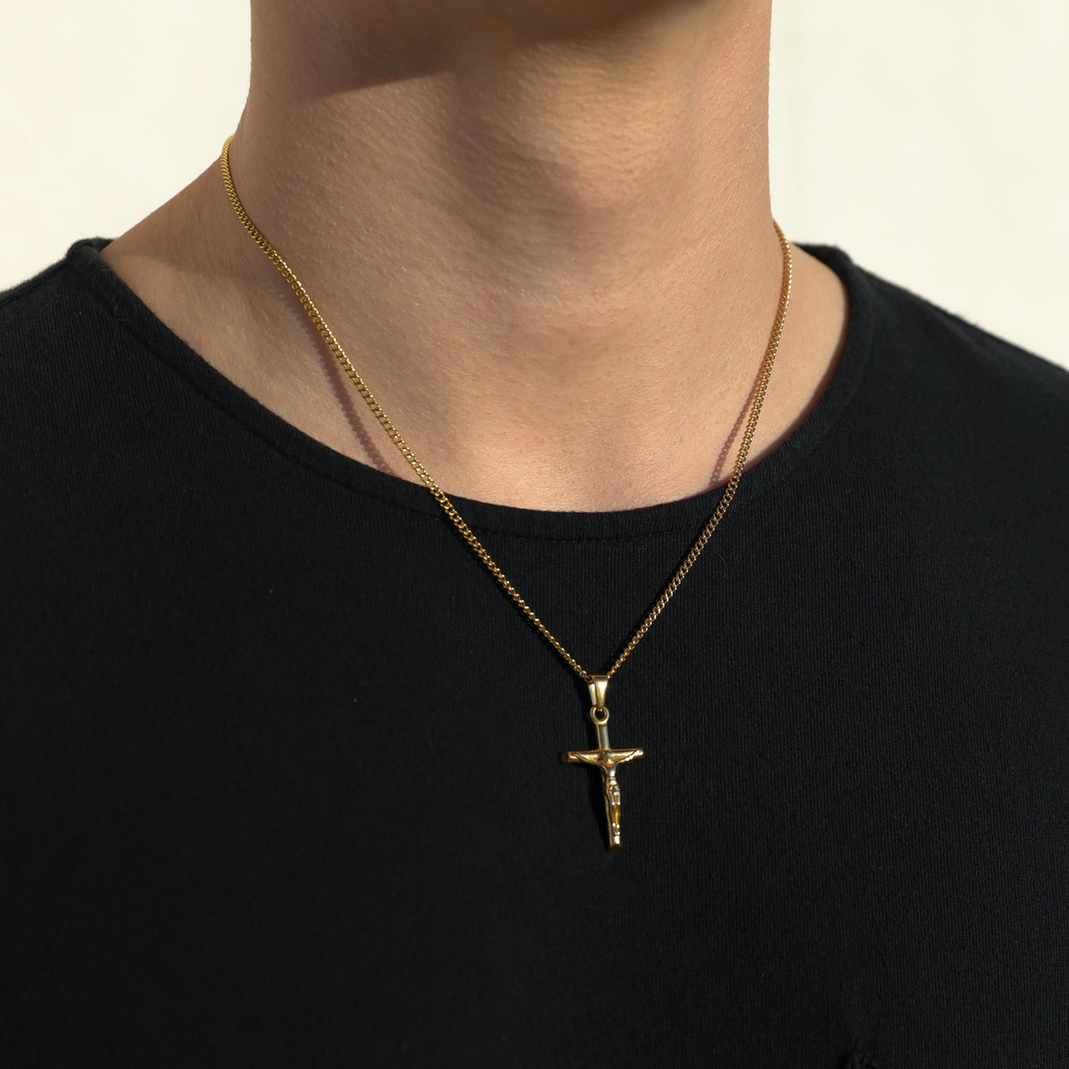 Gold crucifix pendant on figaro chain, centered on neck over black shirt