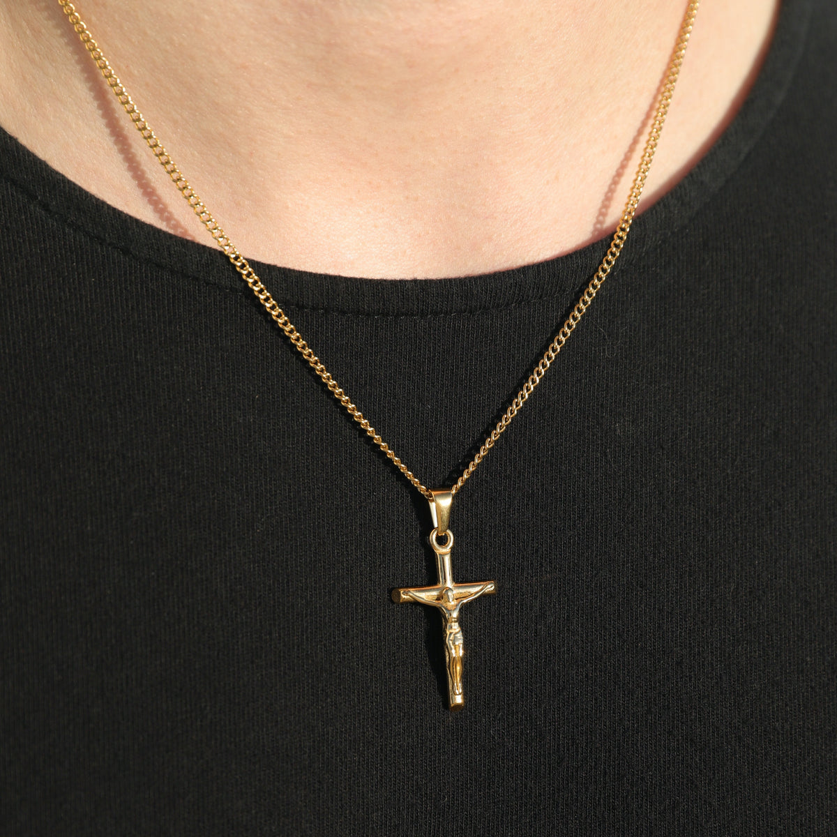 Gold crucifix pendant on curb chain with circular bail, close-up on black shirt