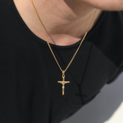 Gold crucifix pendant necklace on thin curb chain, close-up at neckline
