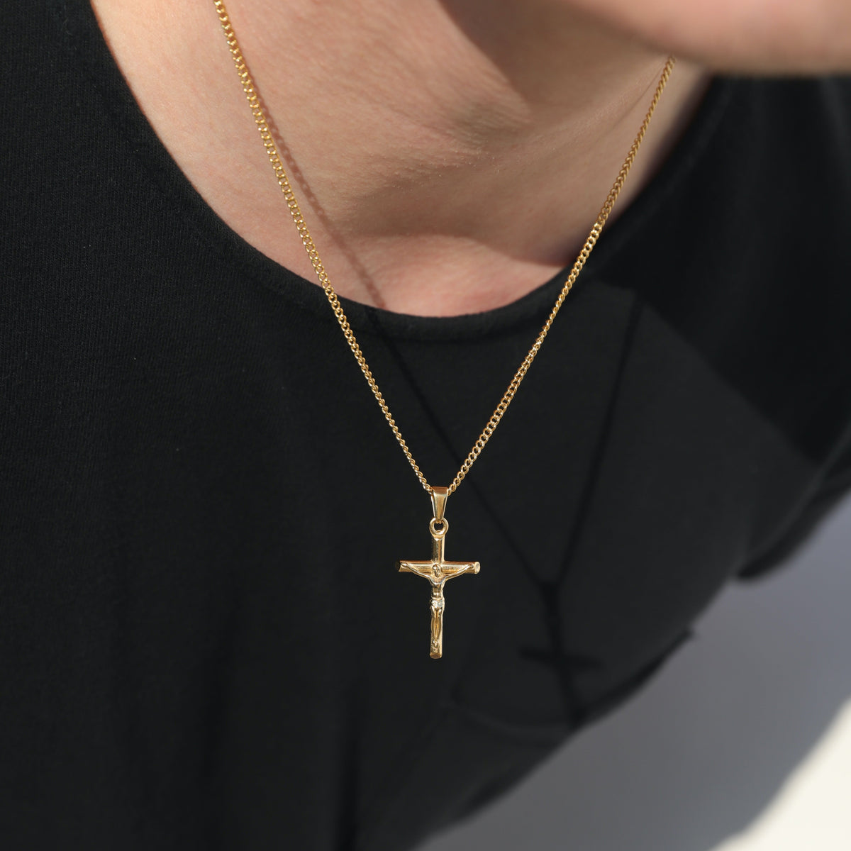 Close-up: gold figaro chain necklace with crucifix pendant on black shirt