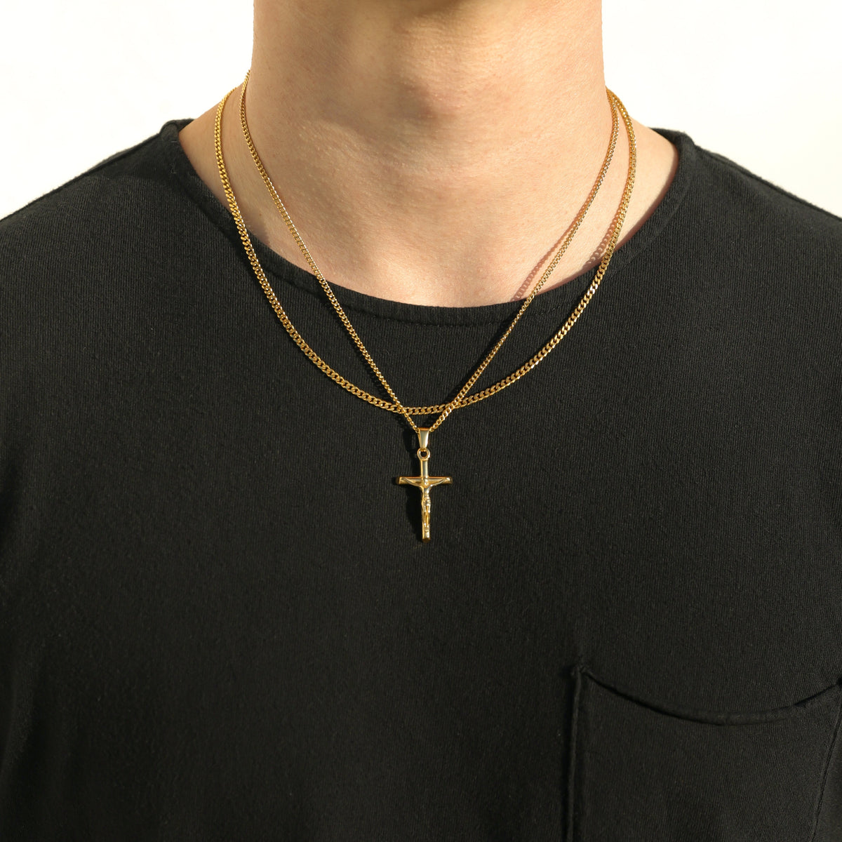 Gold crucifix pendant necklace with curb chain, layered with another chain on neck