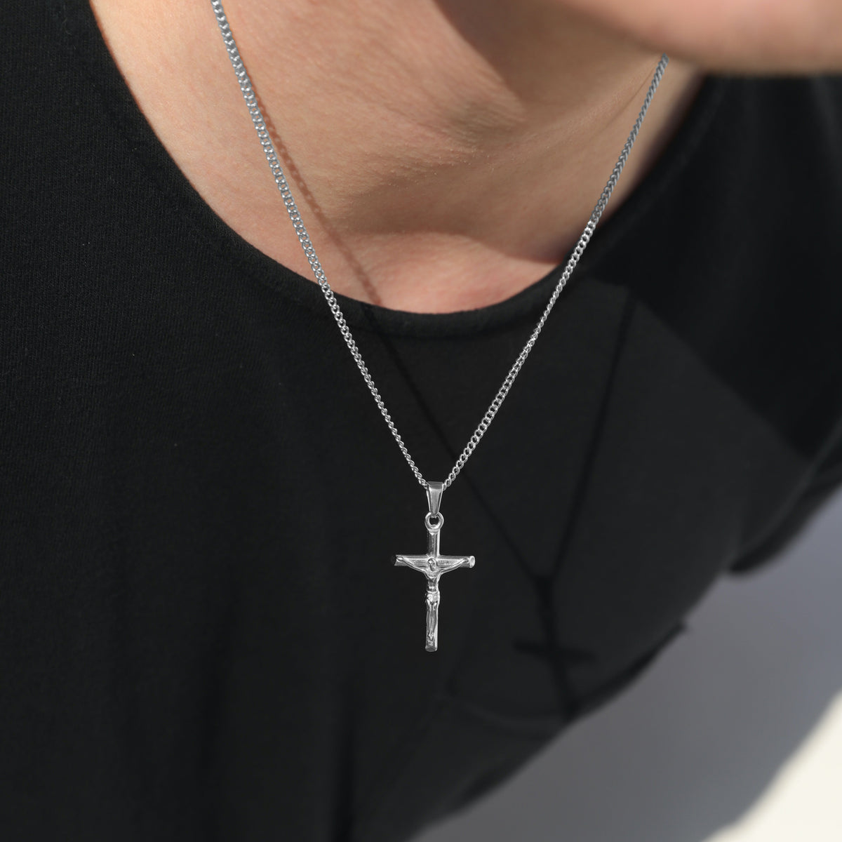 Silver crucifix pendant necklace on curb chain, close-up at neckline on black shirt