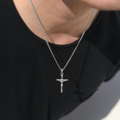 Silver crucifix pendant necklace on curb chain, close-up at neckline on black shirt