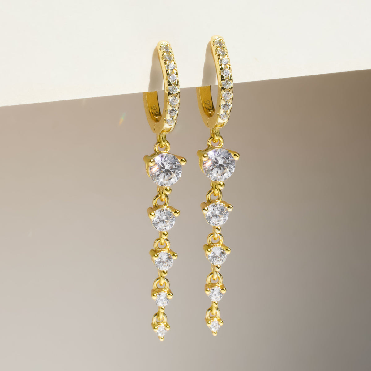 Pair of gold drop hoop earrings with three round clear stones on each earring