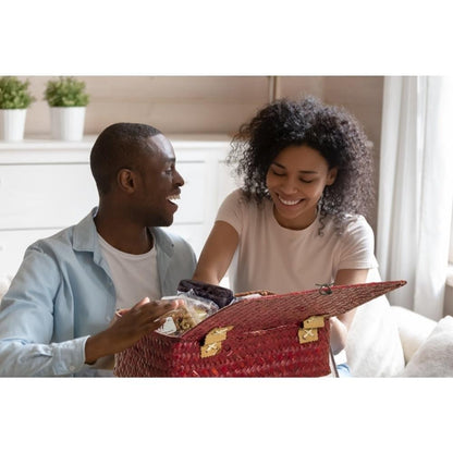 Red woven wicker gift basket held by people indoors, with handle and open top