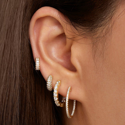 Gold huggie hoop earrings with baguette-cut stones, close-up on ear