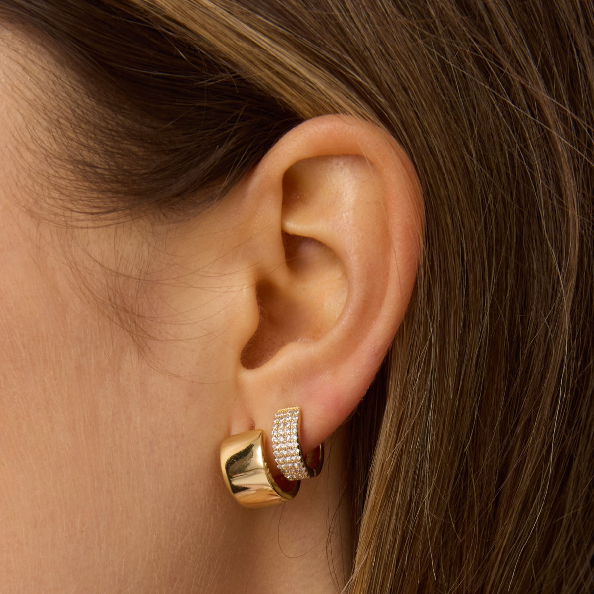 Gold small hoop earring on ear with textured outer band and glossy finish