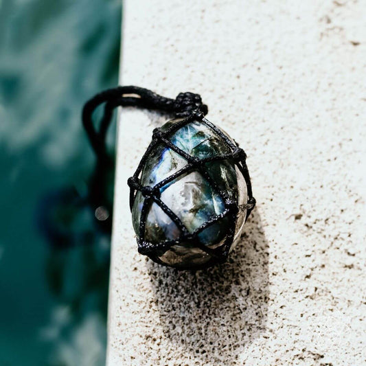Transformation pendant with blue iridescent stone in black wire cage, on dark cord
