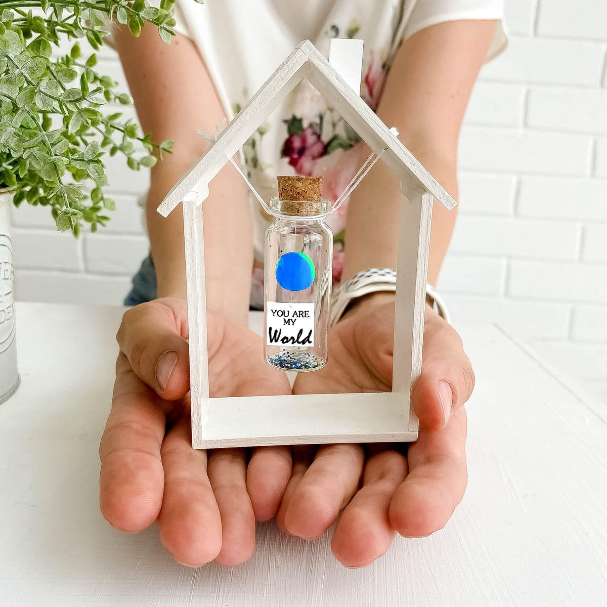 House-shaped frame holding miniature message bottle with cork and small globe design