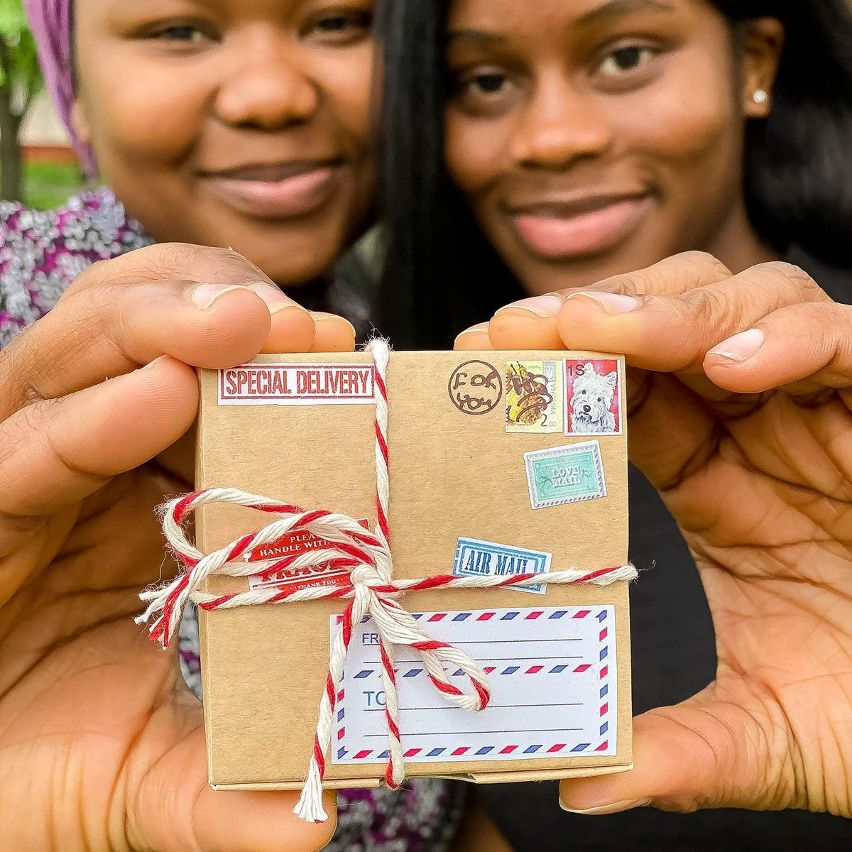 Mini gift box with twine bow and shipping-style stickers held in hands