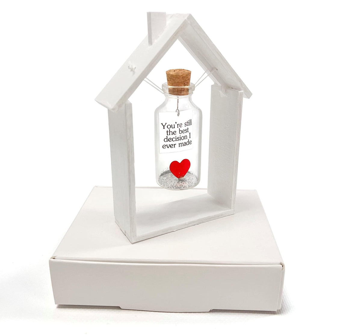 Heart message bottle in white wooden house frame with corked glass bottle and red heart