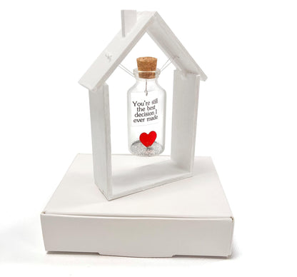 Heart message bottle in white wooden house frame with corked glass bottle and red heart