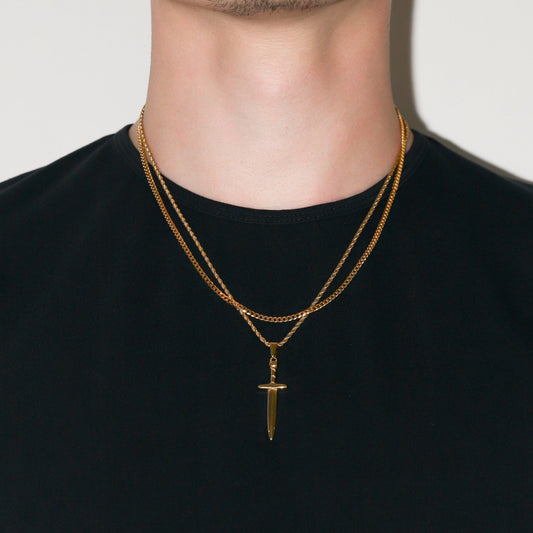 Gold dagger pendant on two-layer Cuban chain necklace set, close view at chest